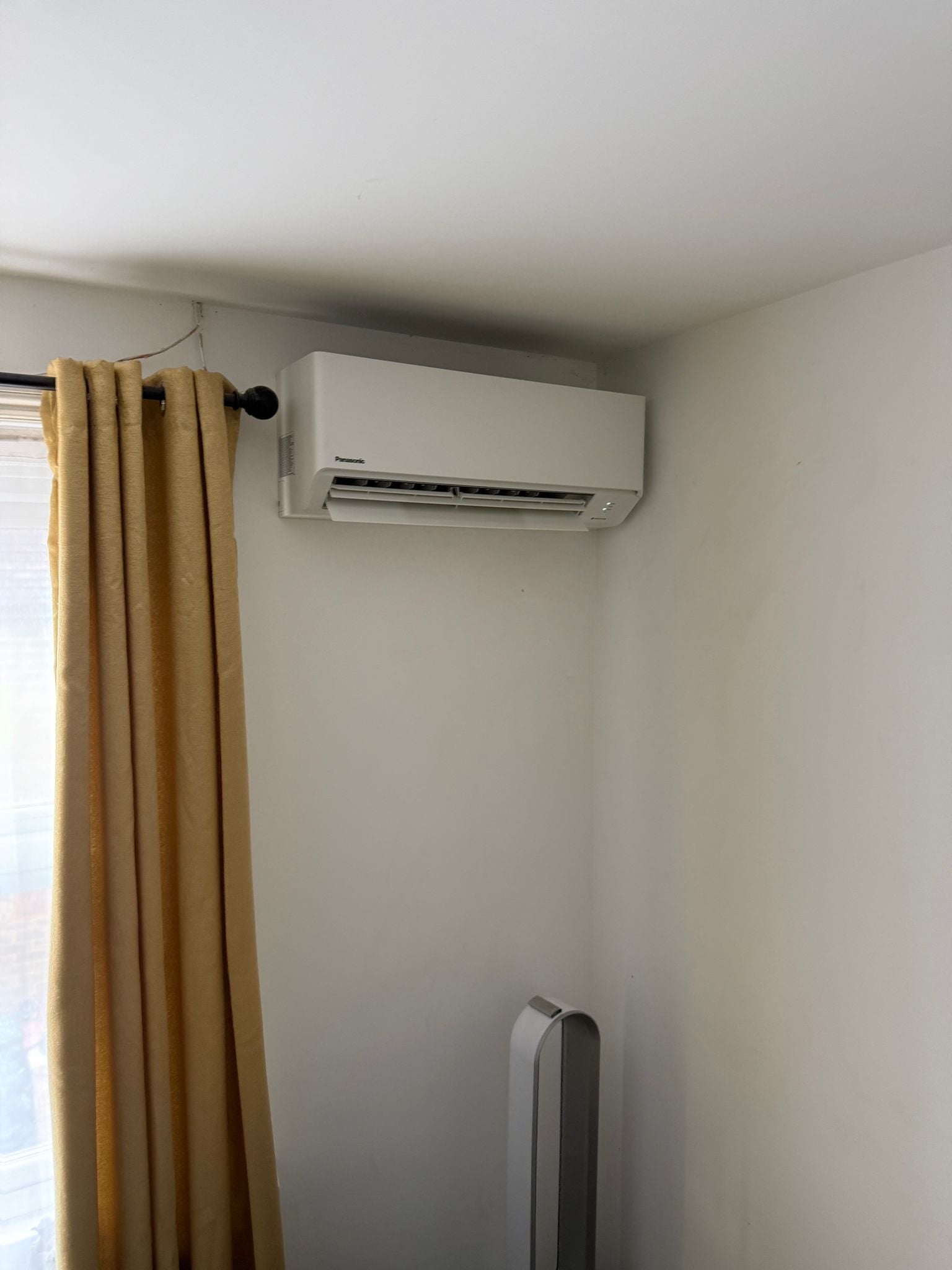 Panasonic wall-mounted air conditioning unit in a bedroom with yellow curtains